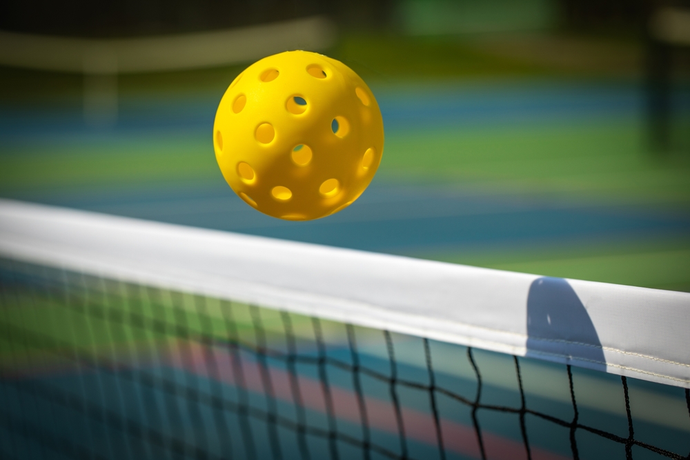Yellow,Pickleball,Crossing,A,Pickleball,Net,With,Shadow,On,The